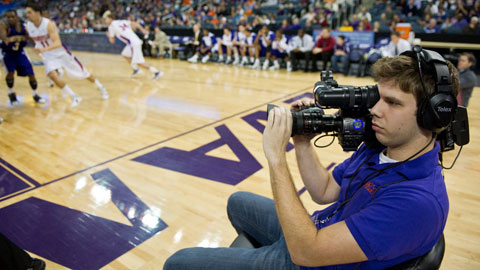 Communication student with camera filming basketball game