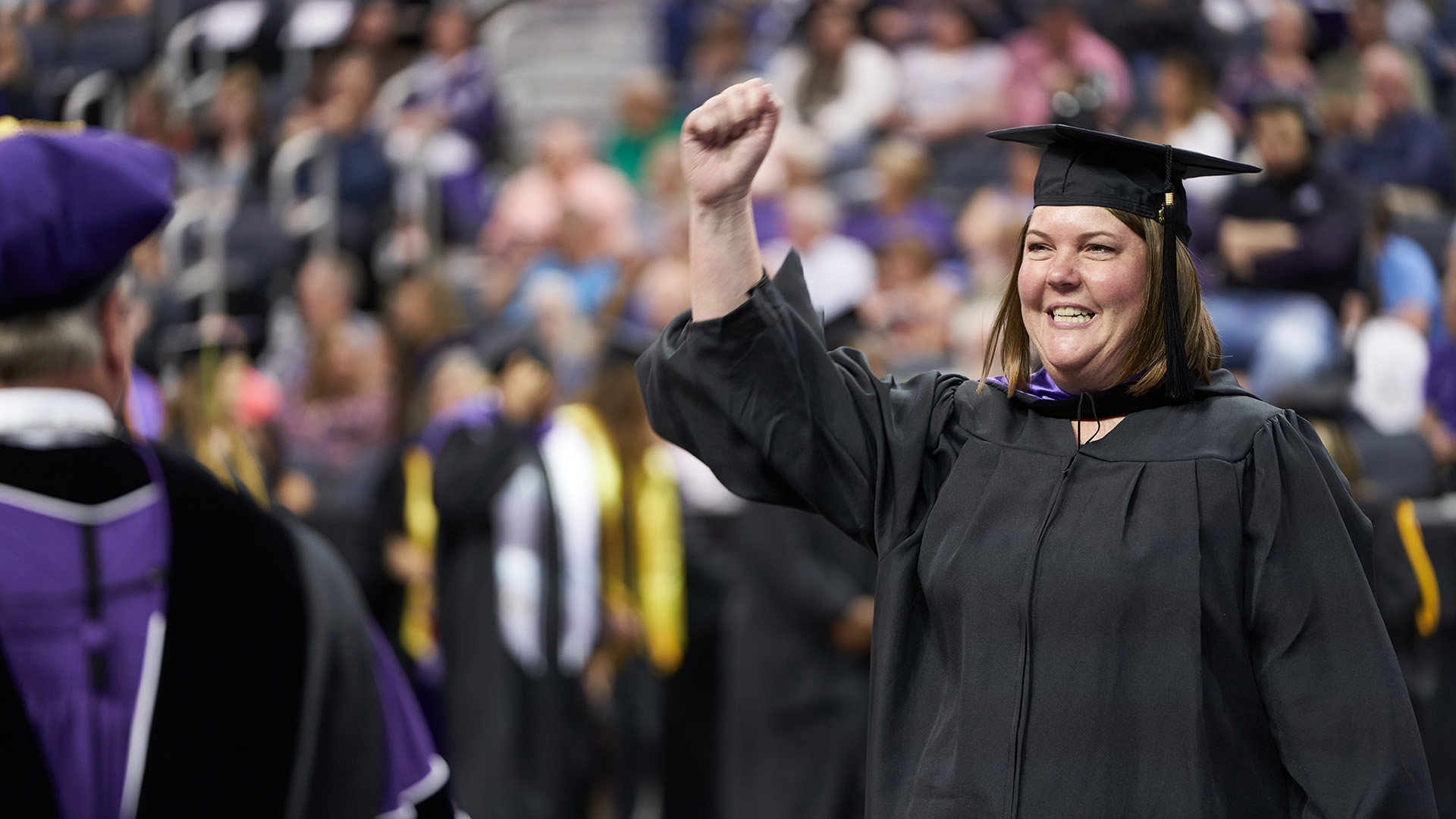 UE adult graduate with hand up at commencement