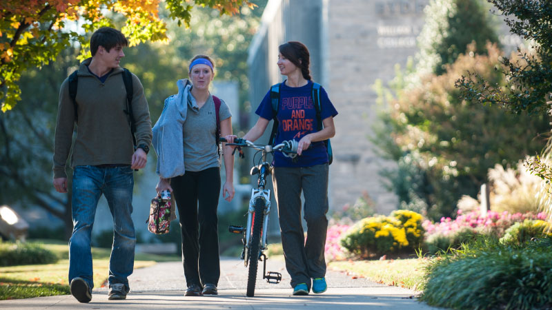 Three students walking with a bike