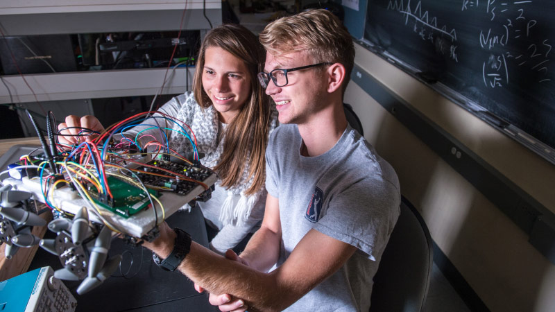 Two engineering students holding up a robot