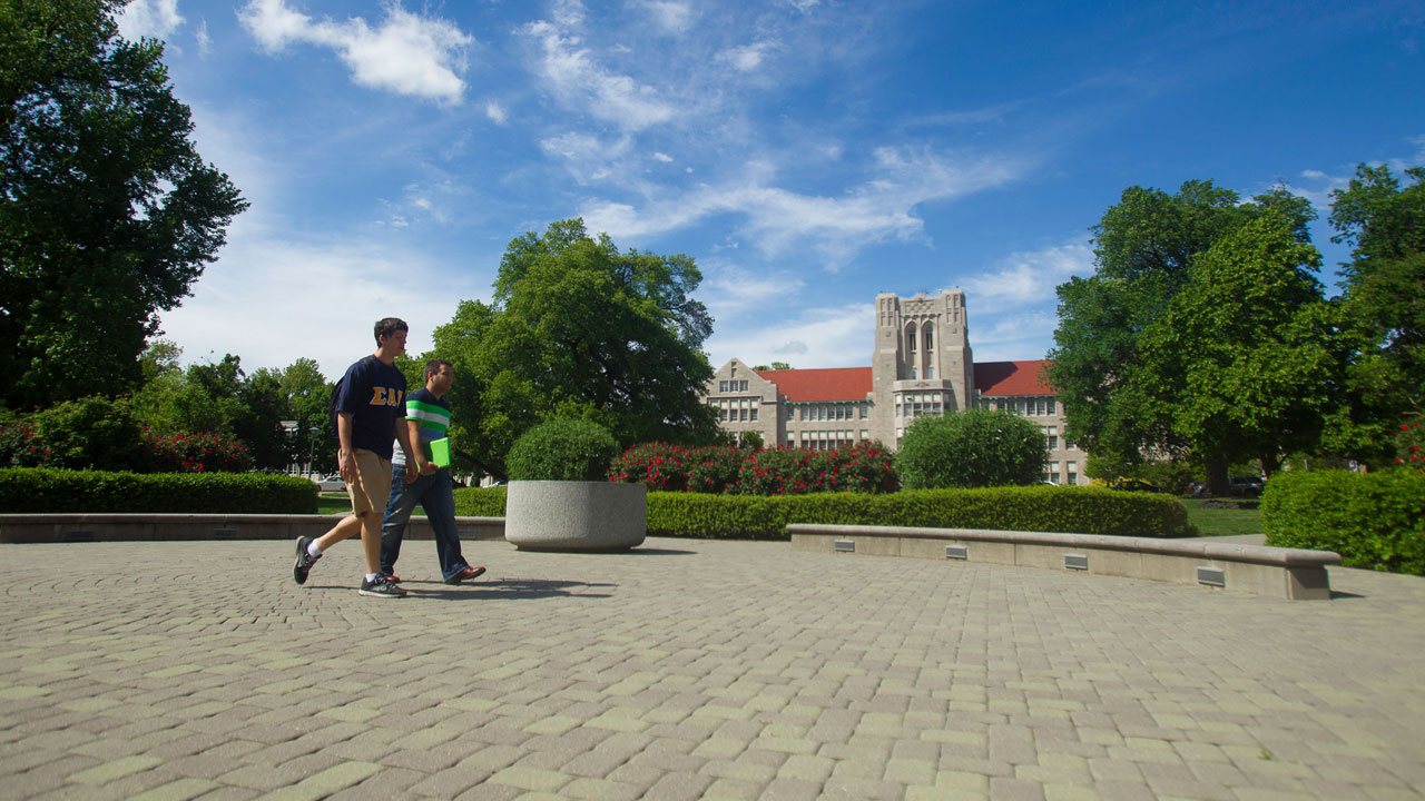Two students walking through the front oval on campus on sunny day.