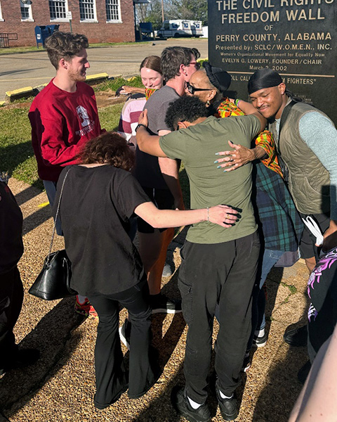 Students and mentor hugging in a huddle at the Civil Rights Freedom Wall