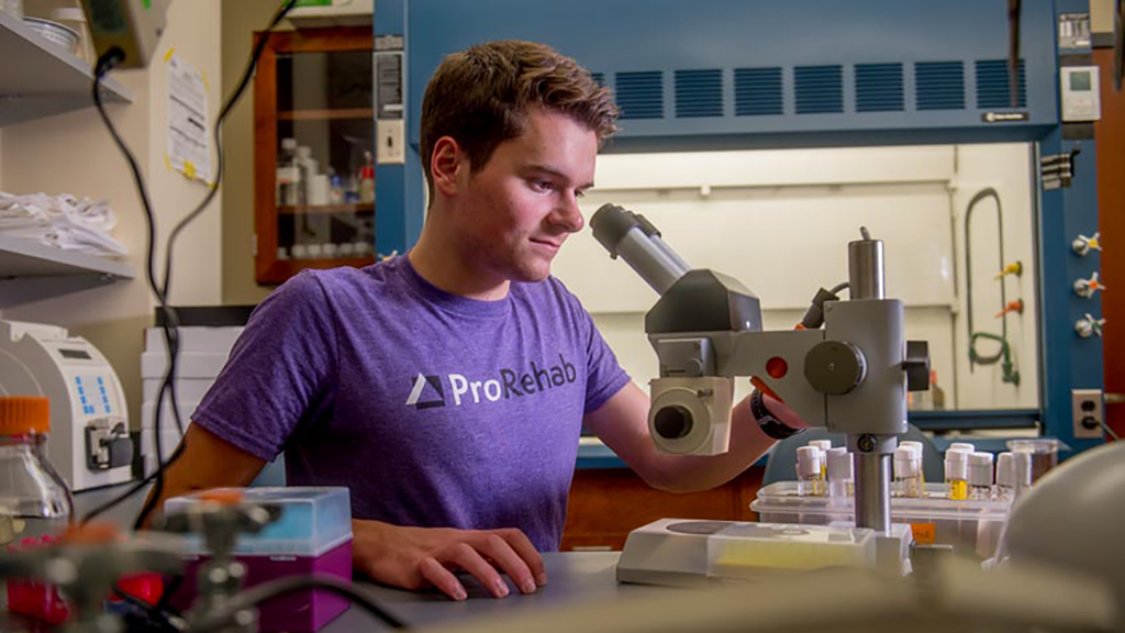 Biology student with microscope in ProRehab t-shirt