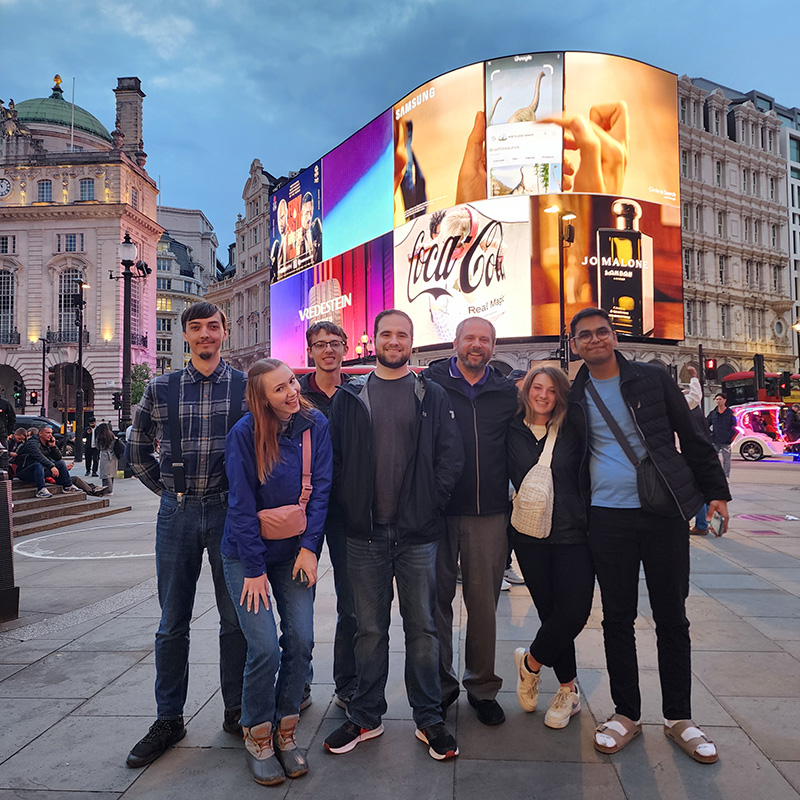 Students standing on street corner with large video screens behind them