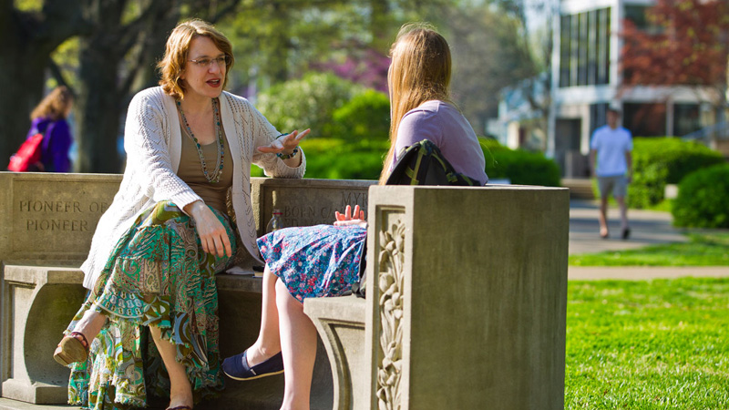 UE faculty member mentoring student outside on bench
