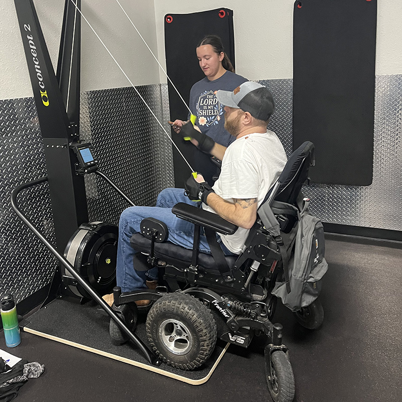 Wheelchair bound spinal cord injury patient performs strength training with help from a UE PT student.