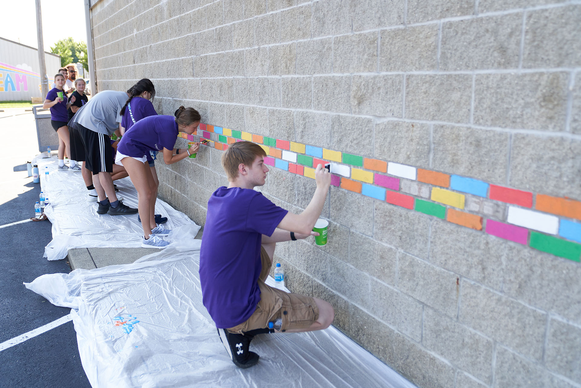 Welcome Week students painting a stone brick wall.